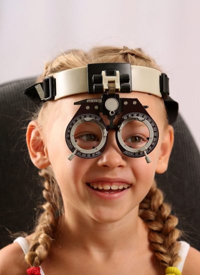 Young girl undergoing eye test with phoropter on blurred background